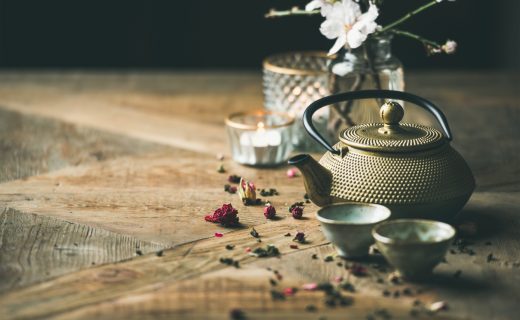 Traditional Asian tea ceremony arrangement. Golden iron teapot, cups, candles and almond blossom flowers over vintage wooden table background, copy space, selective focus